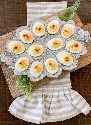 A deviled egg holder elegantly displays filled eggs, viewed from above, set on a striped cloth for entertaining essentials.