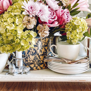 A silver rabbit-shaped candlestick sits among vibrant flowers, viewed from the side, adding charm to the tabletop setting.