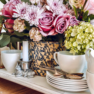 In a cozy tabletop setting, a silver rabbit candlestick holder stands beside elegant floral arrangements.