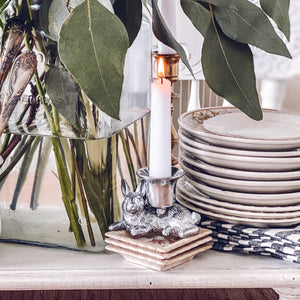 A whimsical rabbit candlestick, viewed from the side, amid stacked plates and lush greenery, ideal for lifestyle home decor.