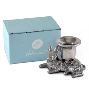 A whimsical Arthur Court candlestick featuring a rabbit design is shown from the side, paired with branded packaging in a soft blue box.