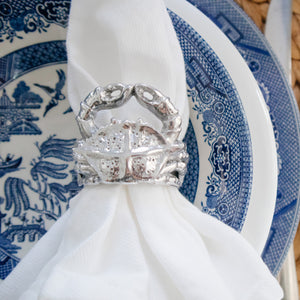 A silver crab napkin ring viewed from above adorns a white napkin, set against blue-patterned china.