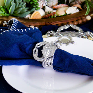 A crab-shaped napkin ring elegantly holds a navy napkin, viewed from a side angle, featuring coastal decor elements.
