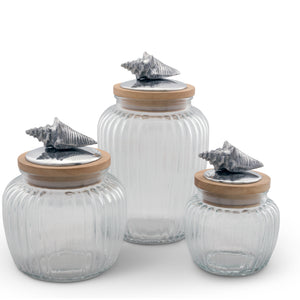 Three glass canisters with wooden lids feature seashell accents, angled to showcase their coastal decor charm.