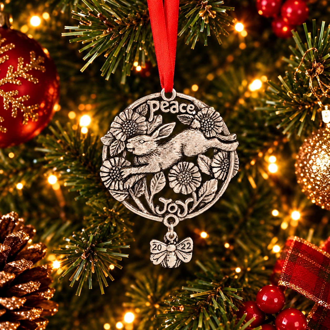 Intricately designed ornament with hare and floral motifs, viewed from above, featuring words "Peace" and "Joy" with a red ribbon.