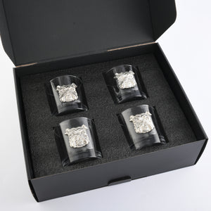 Gift box containing artisan bar glasses with embossed designs, viewed from above, showcasing premium craftsmanship and a luxurious table setting.
