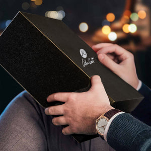 A person holding a sleek black box with a logo, viewed from a side angle, perfect for gifting bar glasses.
