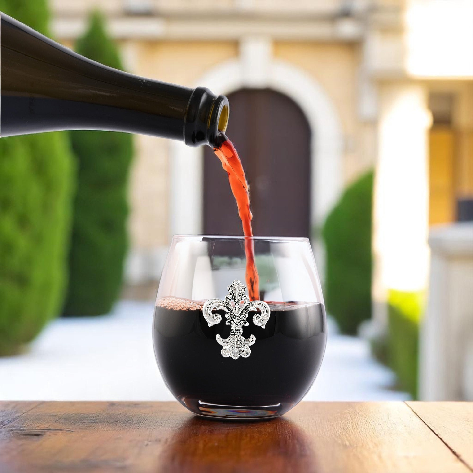 A side view captures wine pouring into a glass adorned with a fleur-de-lis, showcasing artisanal craftsmanship.