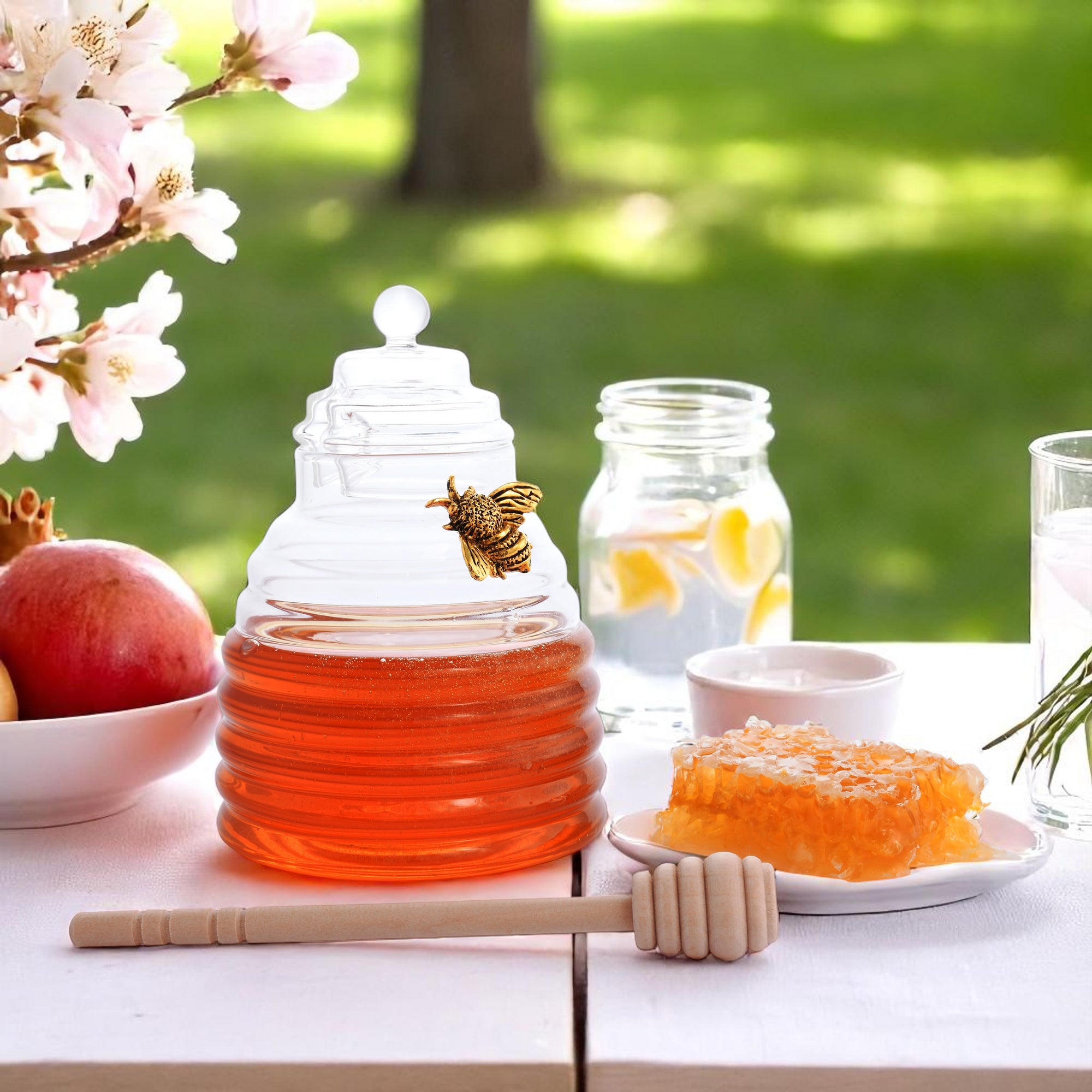 A glass honey pot adorned with a decorative bee is viewed from the side, alongside honeycomb and a wooden dipper.
