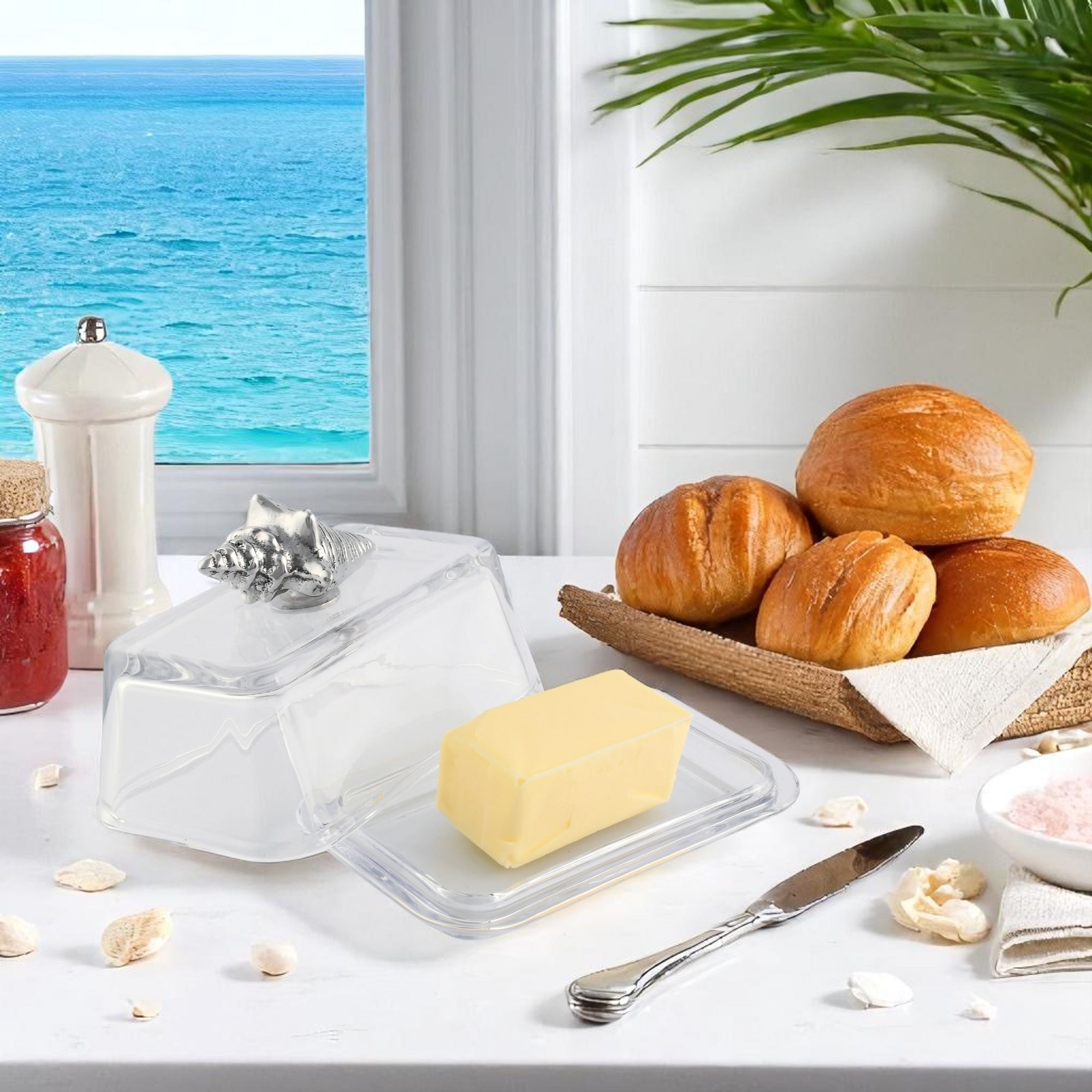 In a side angle, a butter dish with a silver seashell accent elegantly displays butter on a clear tray, perfect for kitchen decor.
