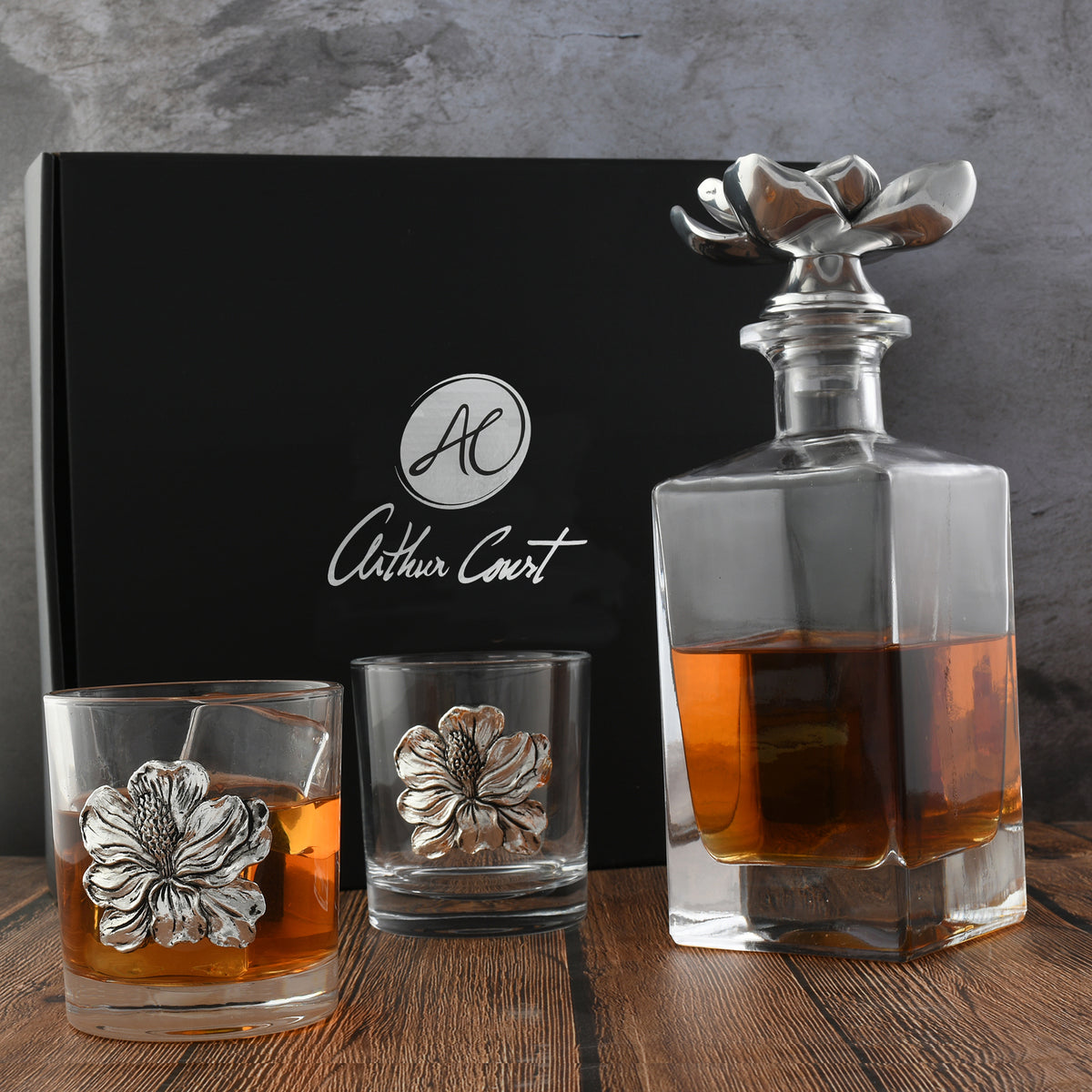 An elegant liquor decanter viewed from the side, with floral-embellished glasses and Arthur Court packaging.