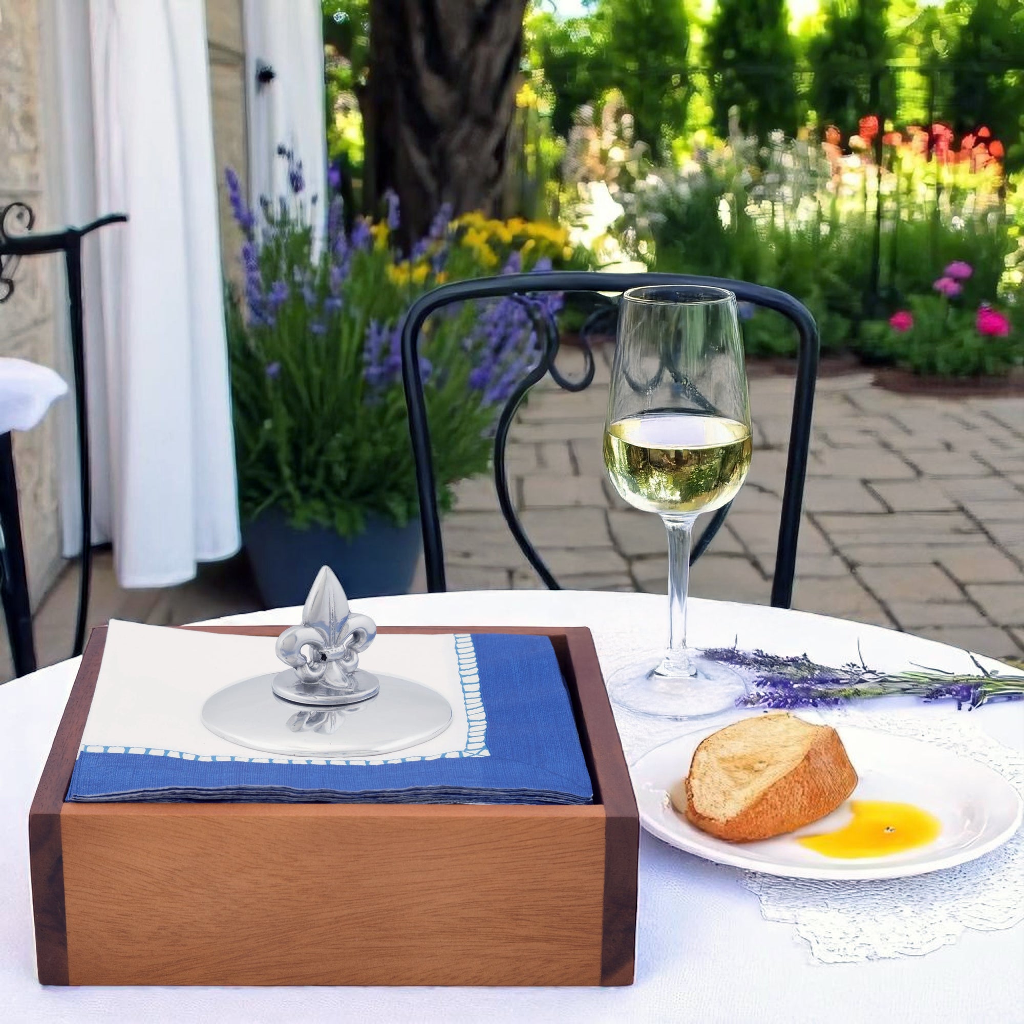 A fleur-de-lis napkin weight elegantly displayed atop blue napkins in a wooden holder, viewed from the side.