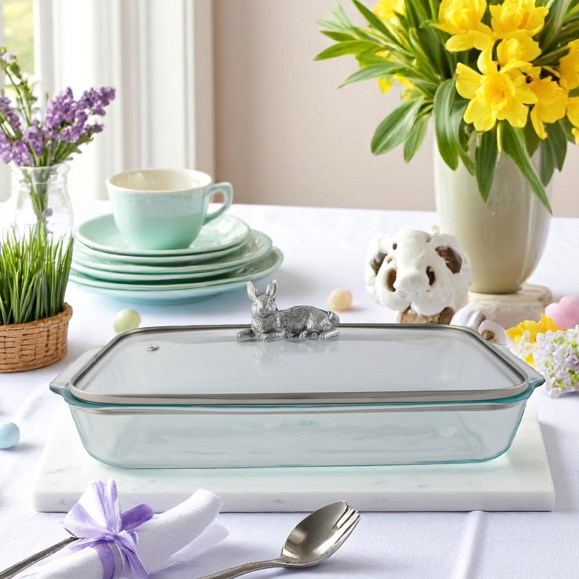 Glass casserole server with a metallic rabbit detail on the lid, angled view highlighting elegant craftsmanship for kitchen decor.