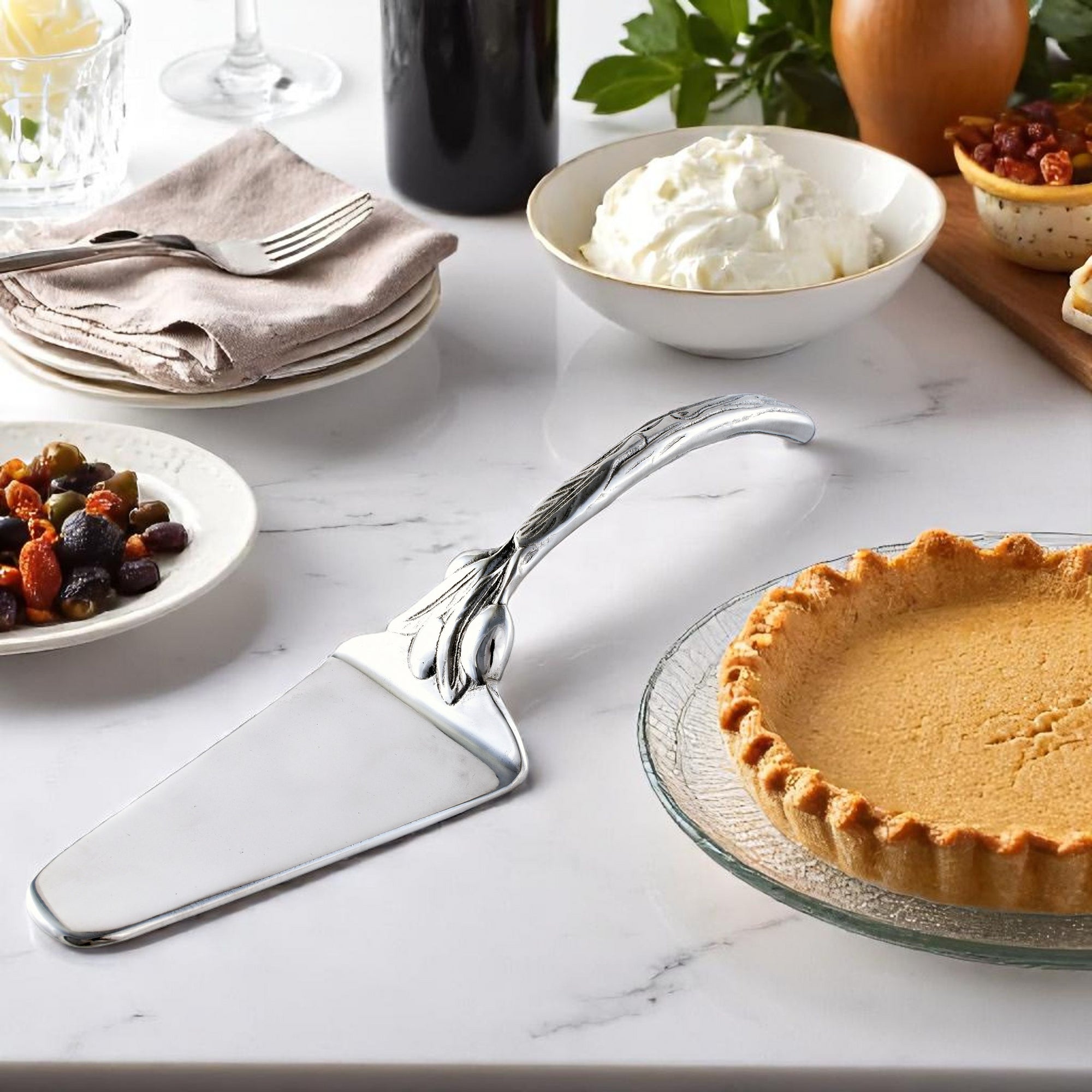 An elegant pie server with ornate handle detailing is viewed from the side on a white background, showcasing artisanal craftsmanship.