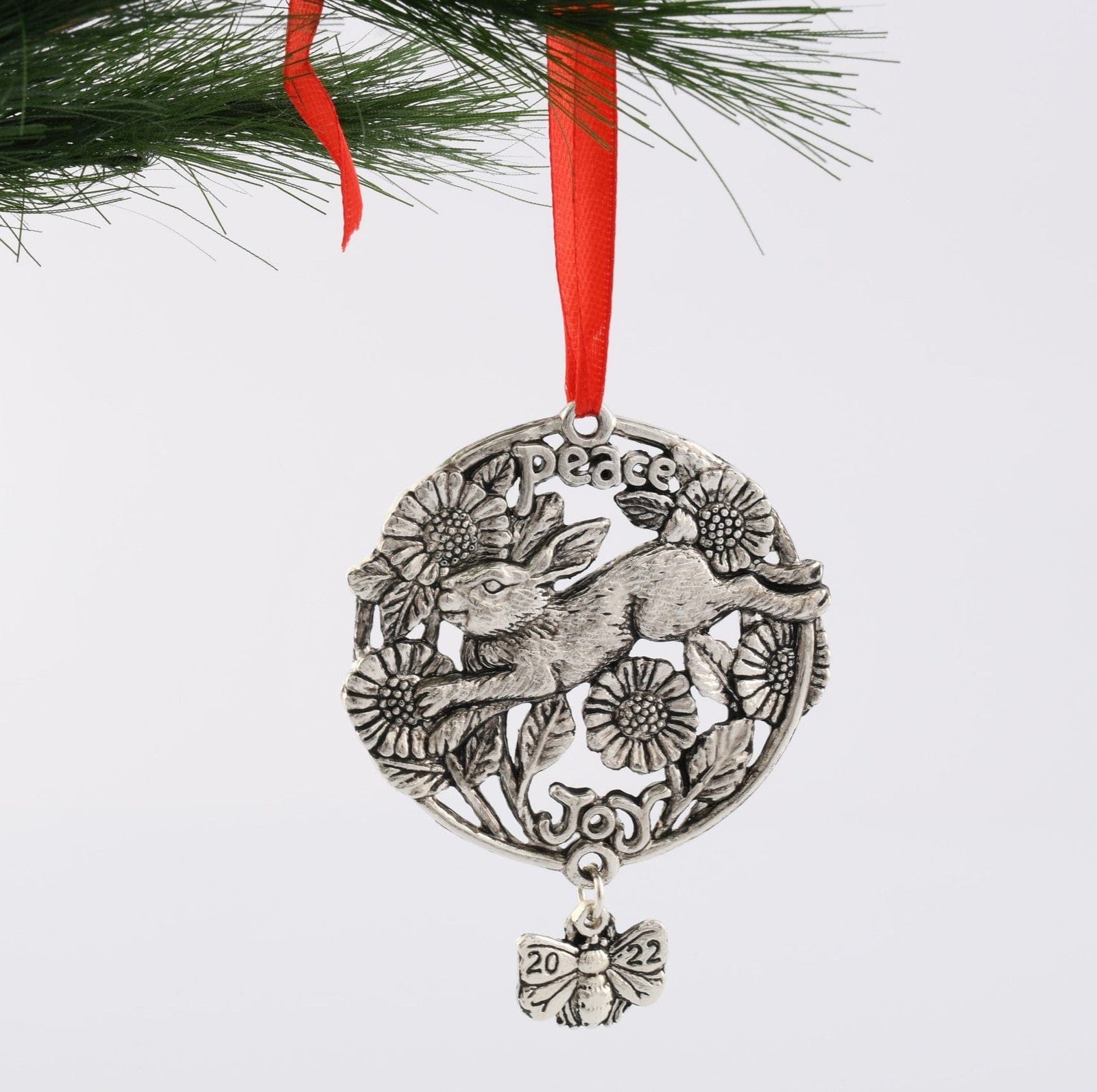 Intricately designed ornament with hare and floral motifs, viewed from above, featuring words "Peace" and "Joy" with a red ribbon.