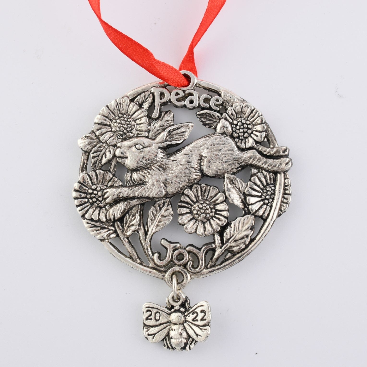 Intricately designed ornament with hare and floral motifs, viewed from above, featuring words "Peace" and "Joy" with a red ribbon.